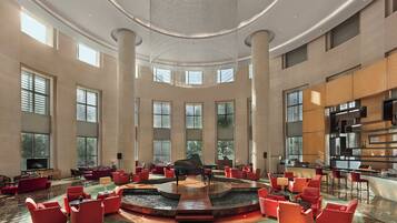 A spacious lobby with a grand piano, multiple seating areas, and large windows.