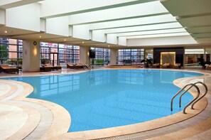 Una gran piscina interior con agua cristalina y azul, rodeada de sillones de descanso y un diseño arquitectónico moderno con grandes ventanales.