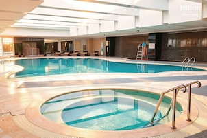 Una piscina con un área hundida, sillas de descanso y una escalera de acceso.