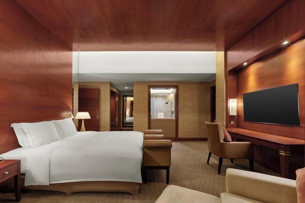 A hotel room with a large bed, a desk, a chair, and a television.