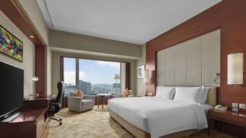 A hotel room with a large bed, a desk, a chair, a TV, and a city view.
