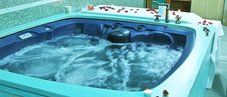 Un jacuzzi con pétalos de rosa y velas, rodeado por un muro de azulejos y paneles de madera.
