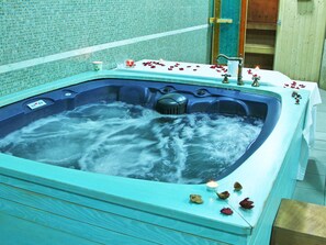 Un bain à remous agrémenté de pétales de rose et de bougies, entouré d’un mur carrelé et d’un lambris en bois.