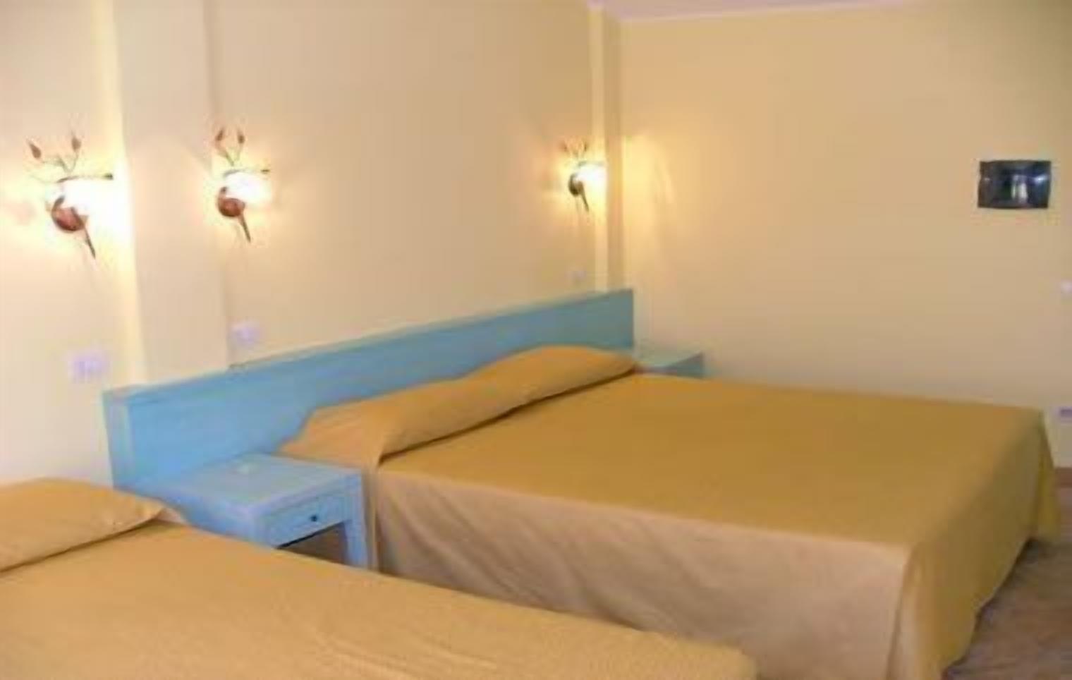 Une chambre d’hôtel avec deux lits, chacun doté d’une tête de lit bleue et d’une literie beige. Des lampes murales sont fixées au-dessus de chaque lit.