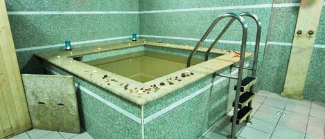 Un cuarto de spa con una bañera de hidromasaje rectangular, paredes de azulejos y un banco de madera.