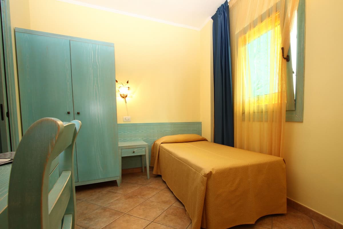 A small, single-room hotel room with a bed, a desk, and a chair.