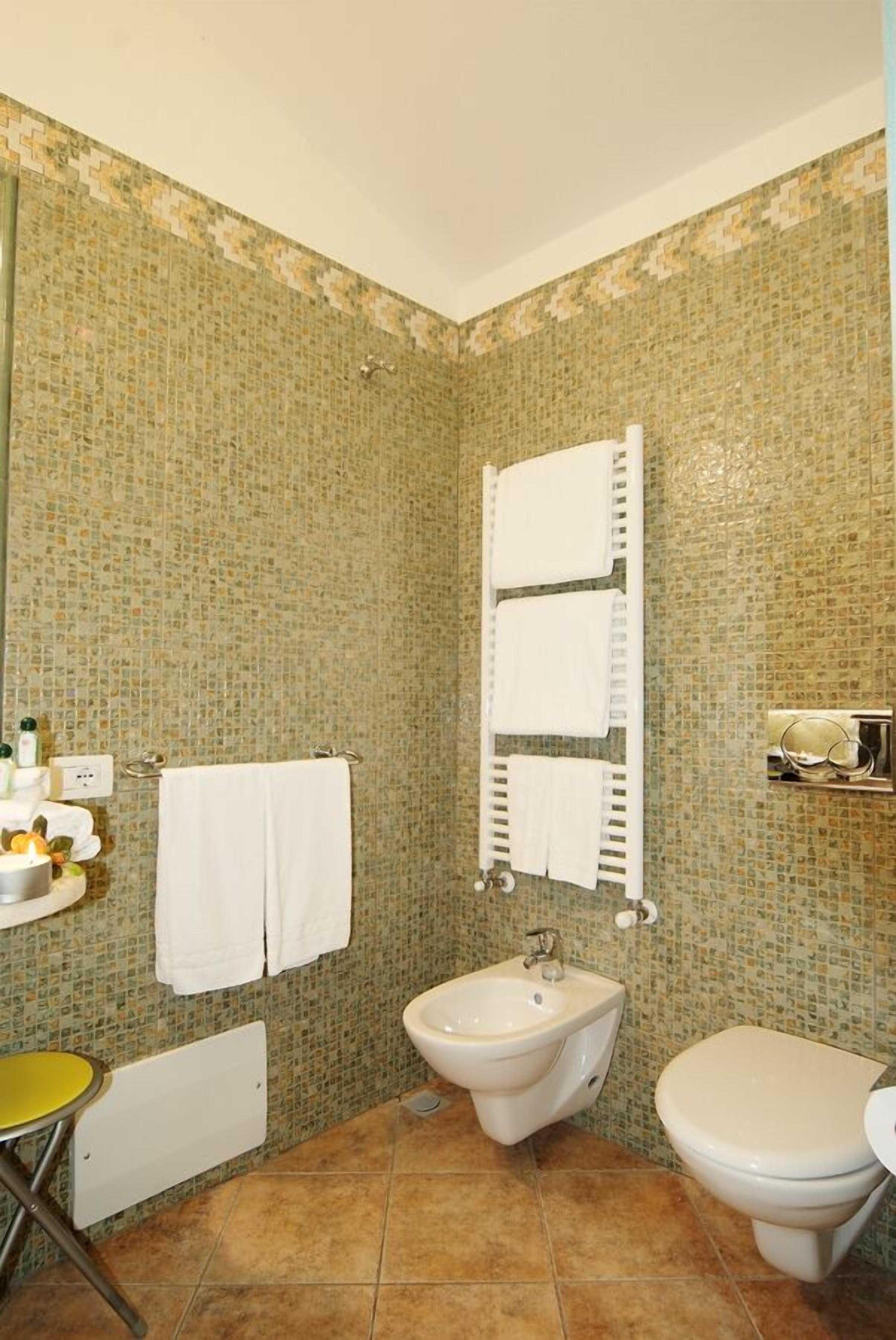 A bathroom with mosaic tile walls, a bidet, a toilet, and a small table with toiletries.