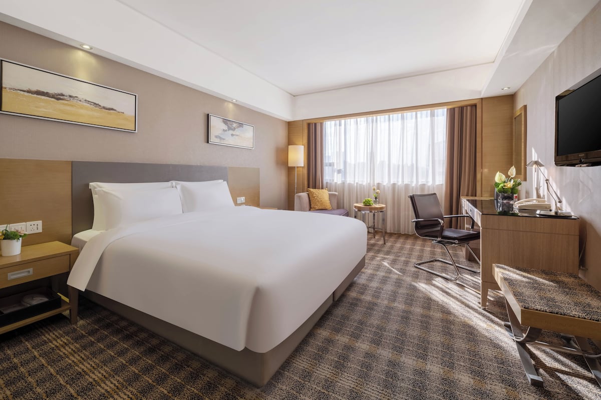 A hotel room with a large bed, a desk with a chair, a TV, and a window with curtains.