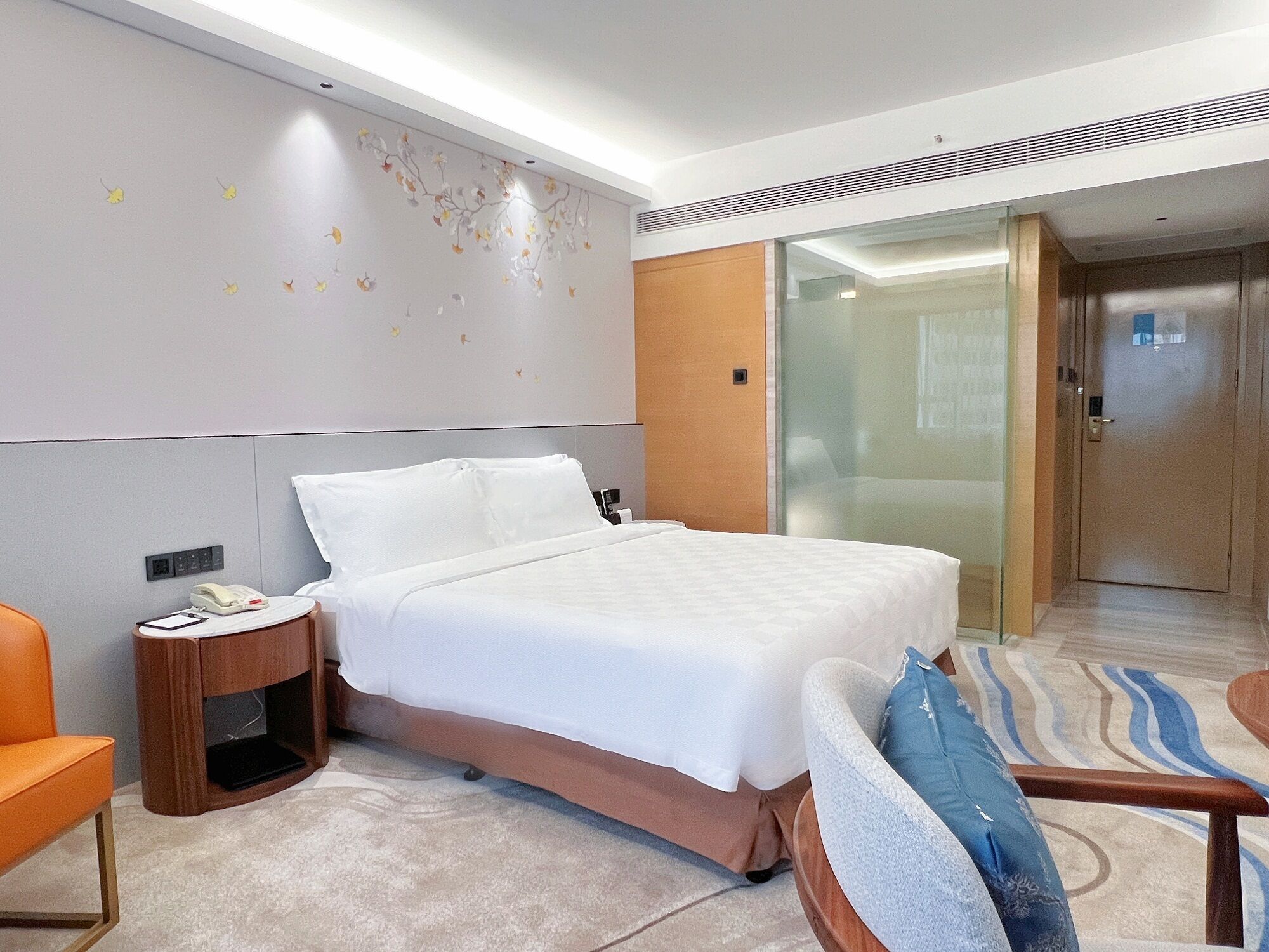 Una habitación de hotel moderna con una cama grande, una mesita de noche de madera, un teléfono y una silla.
