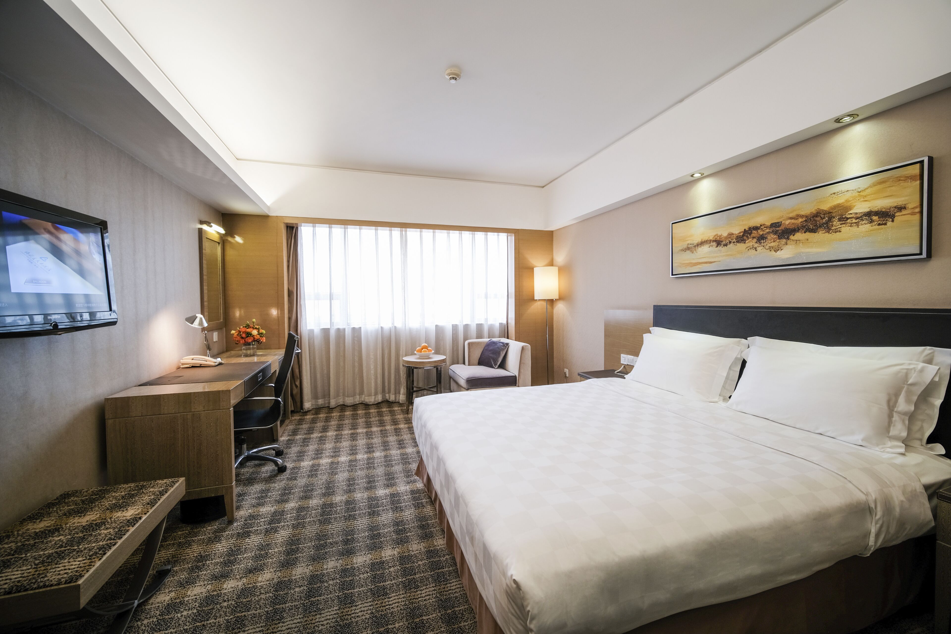 A hotel room with a large bed, a desk with a chair, a television, and a window with curtains.
