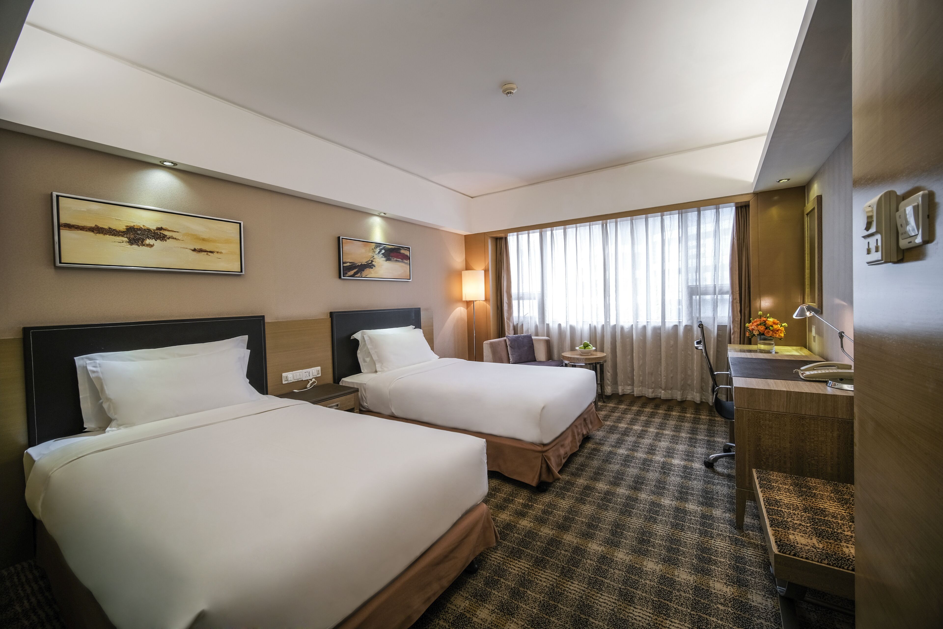 A hotel room with two beds, a desk, a chair, a lamp, and a large window with curtains.