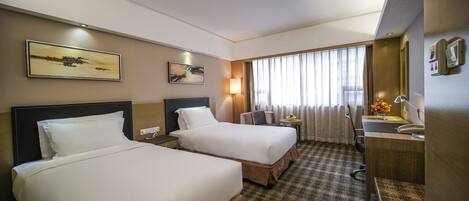 A hotel room with two beds, a desk, a chair, a lamp, and a large window with curtains.