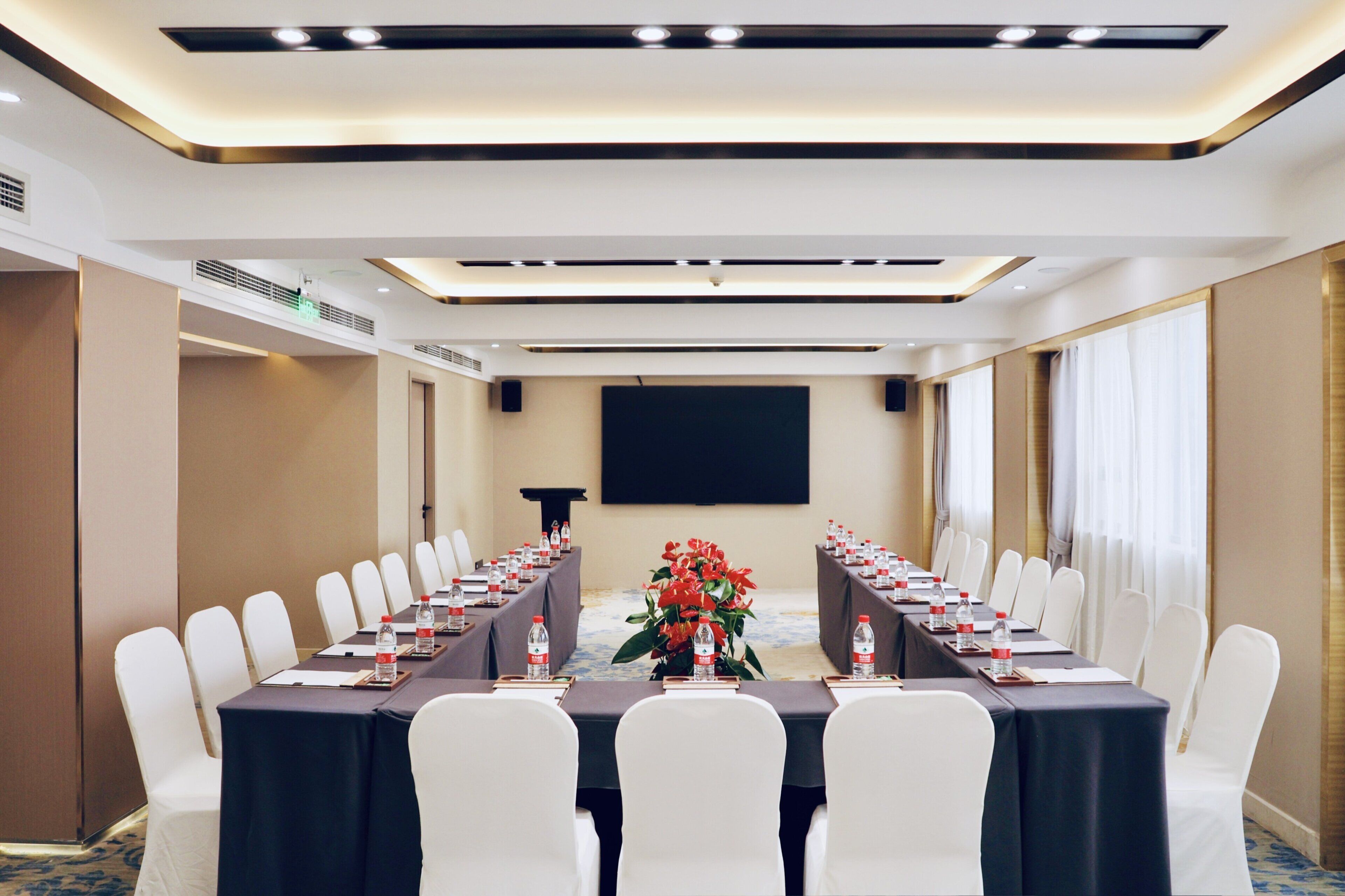 A conference room with a long table, white chairs, and a projector screen.