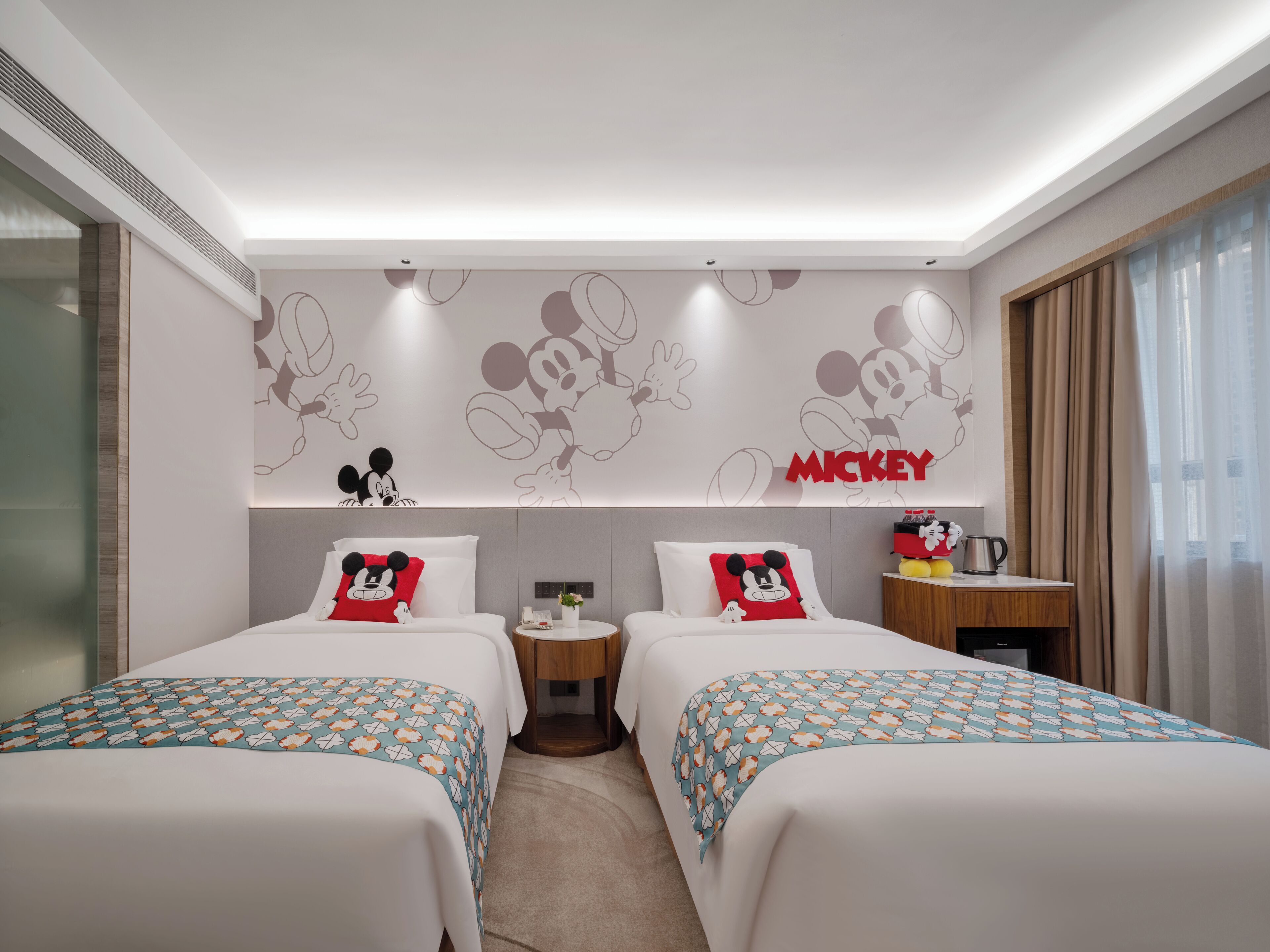 A hotel room with two beds, a Mickey Mouse themed wall, and a small side table with a coffee pot.