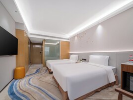 A hotel room with two beds, a flat-screen TV, a bedside table with a bottle, and a wall-mounted heater.