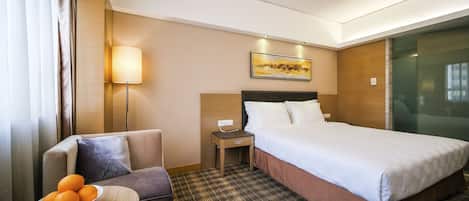 A hotel room with a bed, a nightstand, a lamp, a sofa, and a table with oranges.