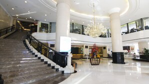 Um hall espaçoso com uma escadaria imponente, grandes colunas e um candelabro.