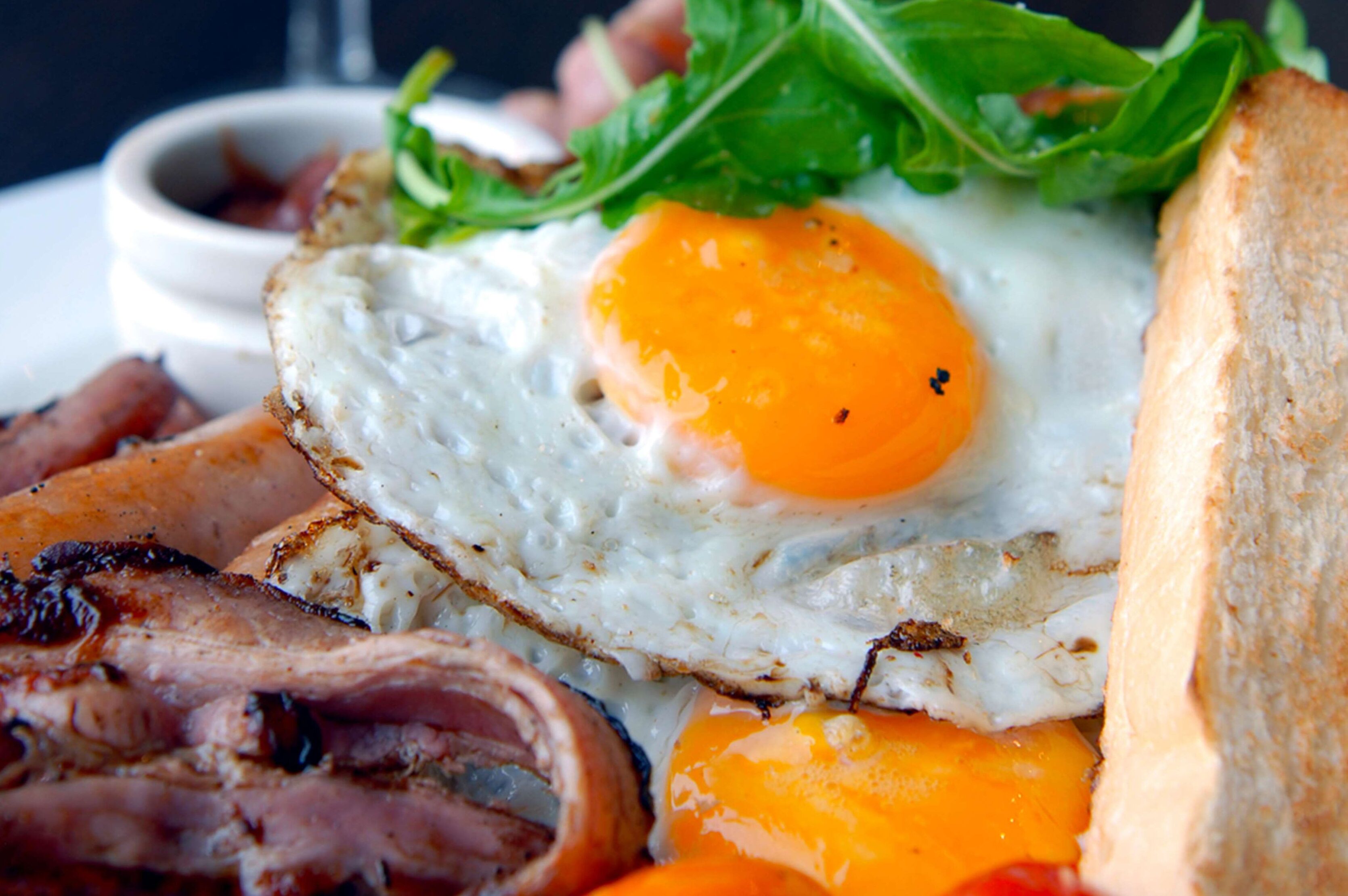 Ein Frühstücksteller mit Spiegeleiern, Speck, Toast und Grünzeug.