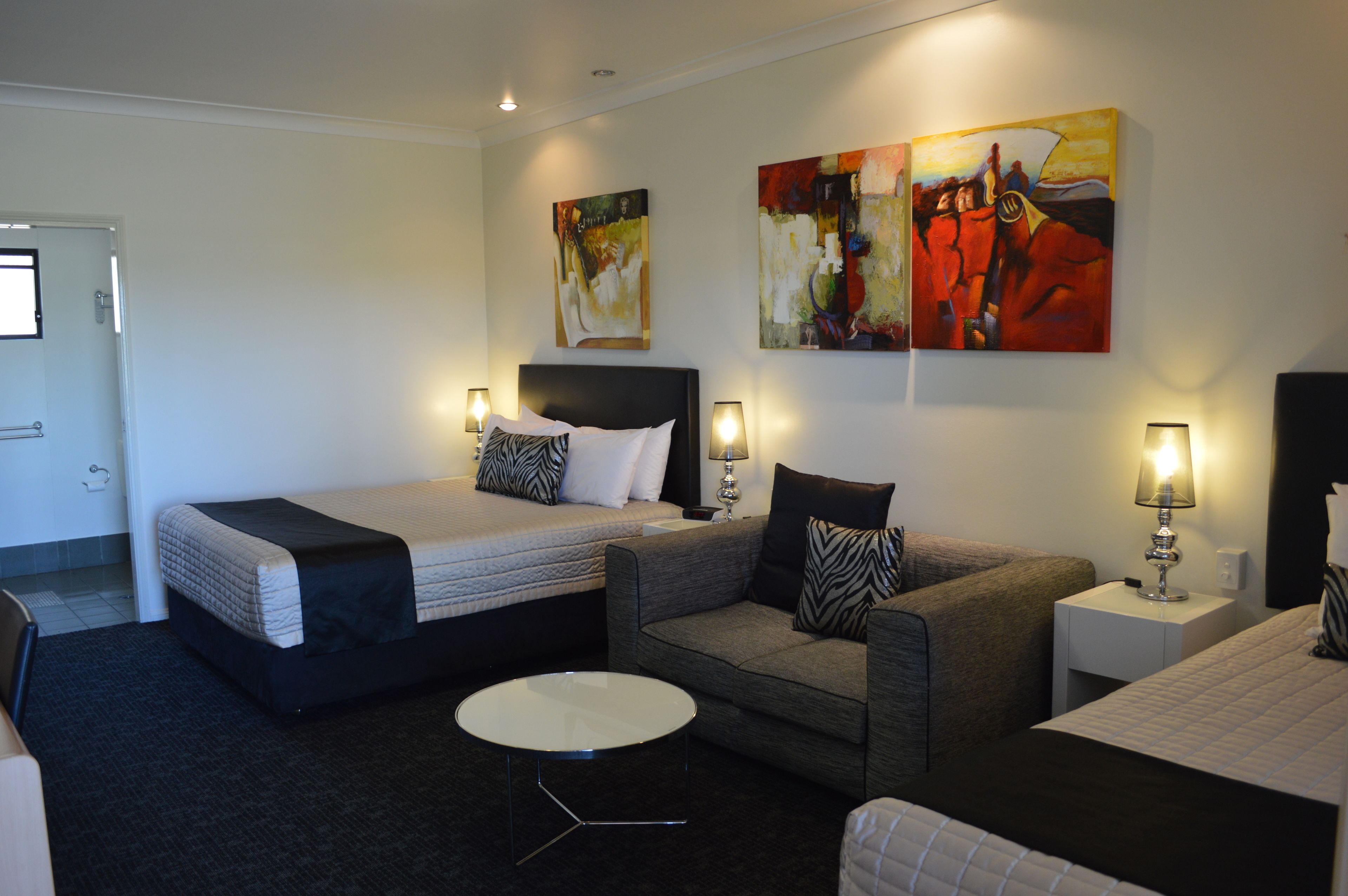 A hotel room with a bed, a sofa, a small table, and two nightstands with lamps. There are two paintings on the wall.