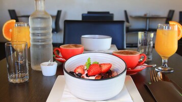 Una mesa de desayuno con ensalada de frutas, jugo de naranja y tazas de café.