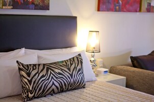 Una cama bien hecha con un cojín estampado de cebra, una lámpara de noche y un sofá marrón en una habitación de hotel.