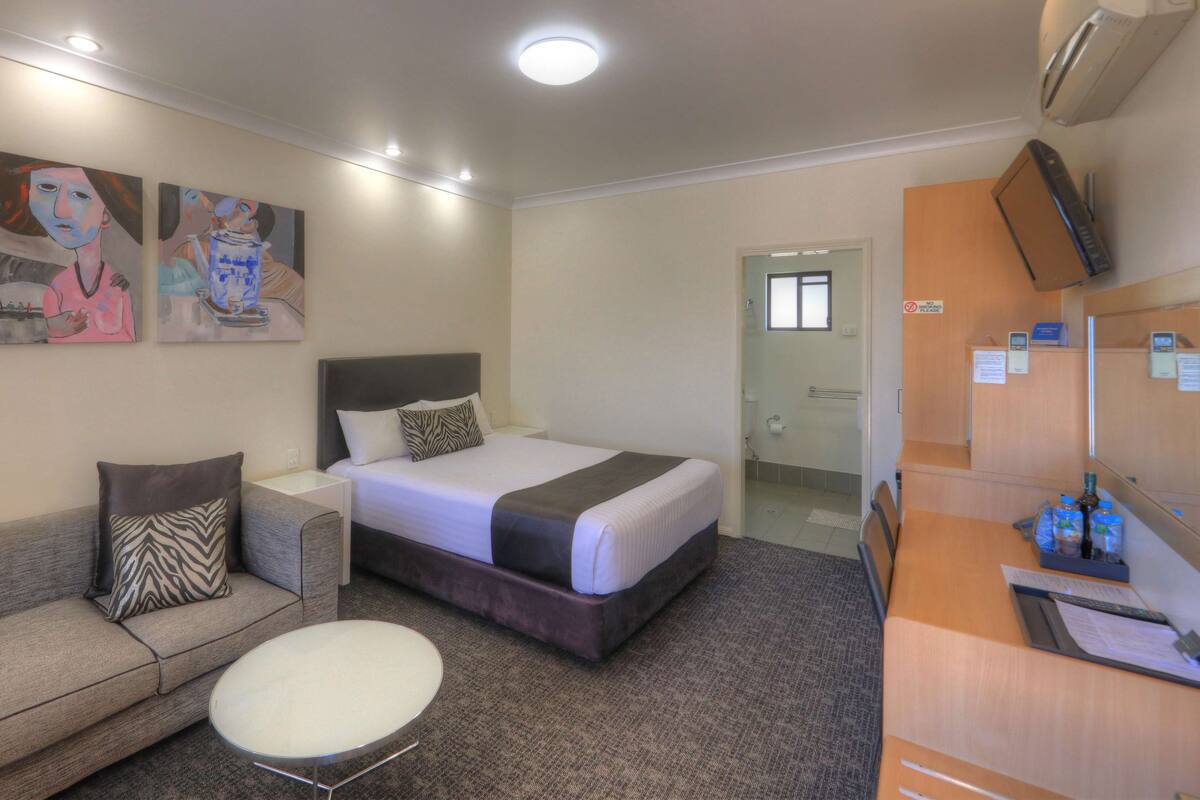 A hotel room with a bed, a sofa, a small table, and artwork on the wall.