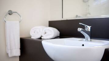 A modern bathroom with a white sink, a dark countertop, and a towel rack with rolled towels.