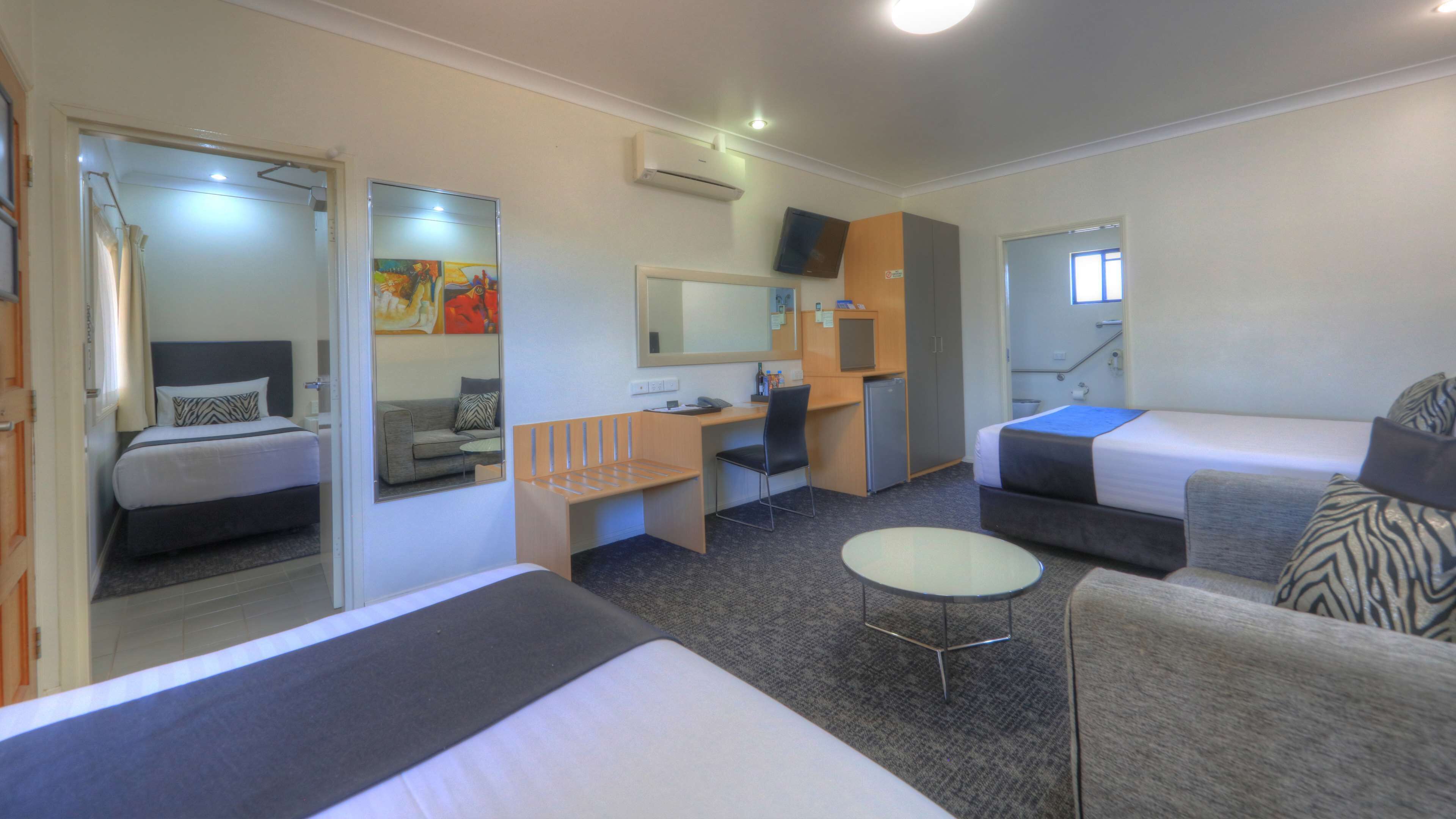 Een kleine hotelkamer met een bed, een bureau, een stoel, een tafeltje, een spiegel en een televisie.