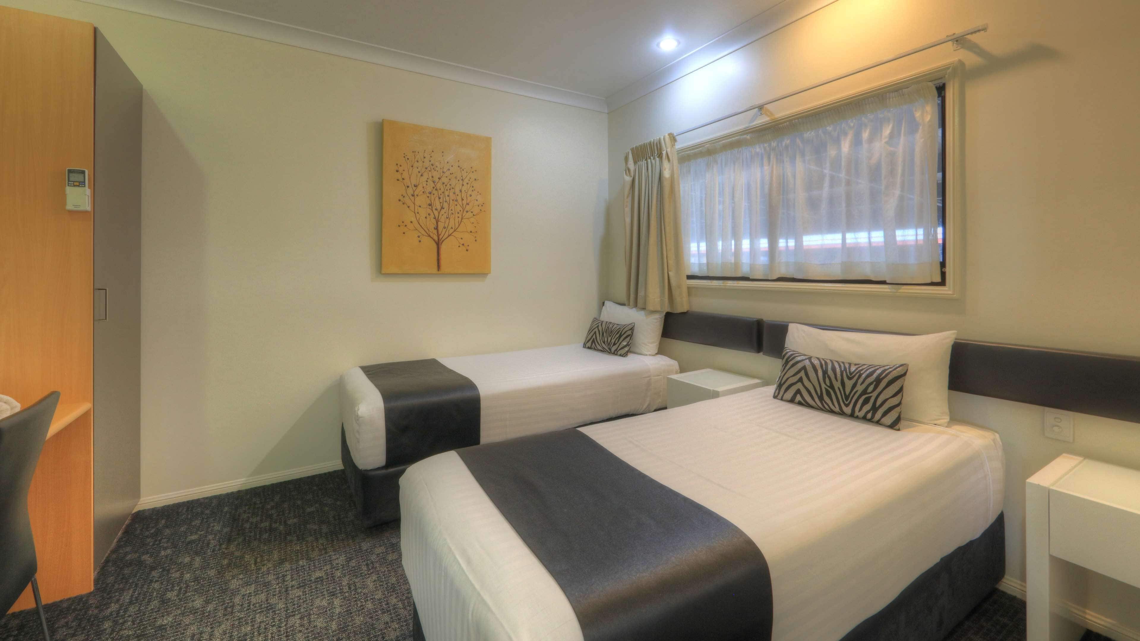 A hotel room with two beds, a desk, a chair, a painting, and a window with curtains.