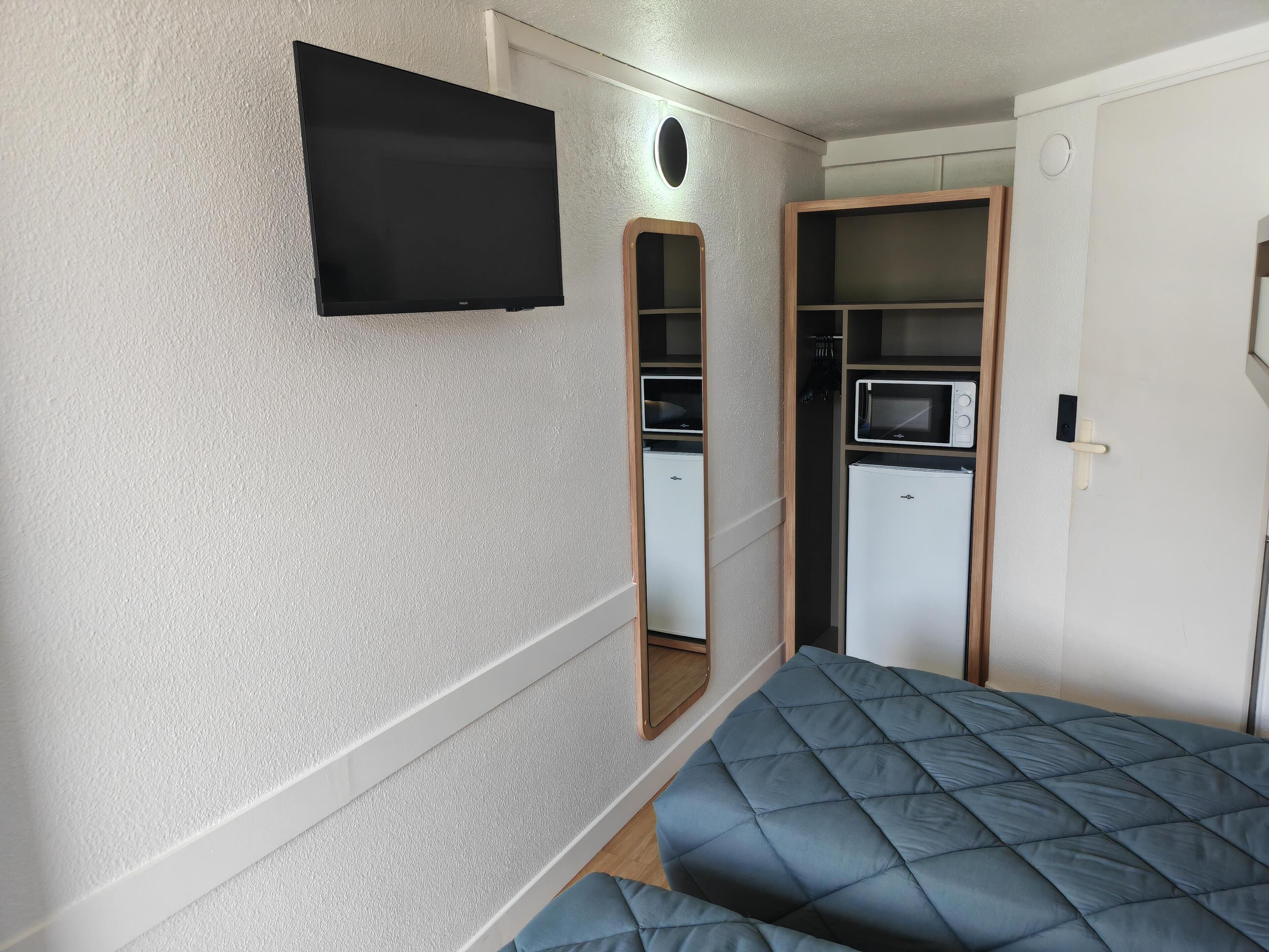 A compact room with a bed, a TV, a small kitchenette, and a wardrobe.