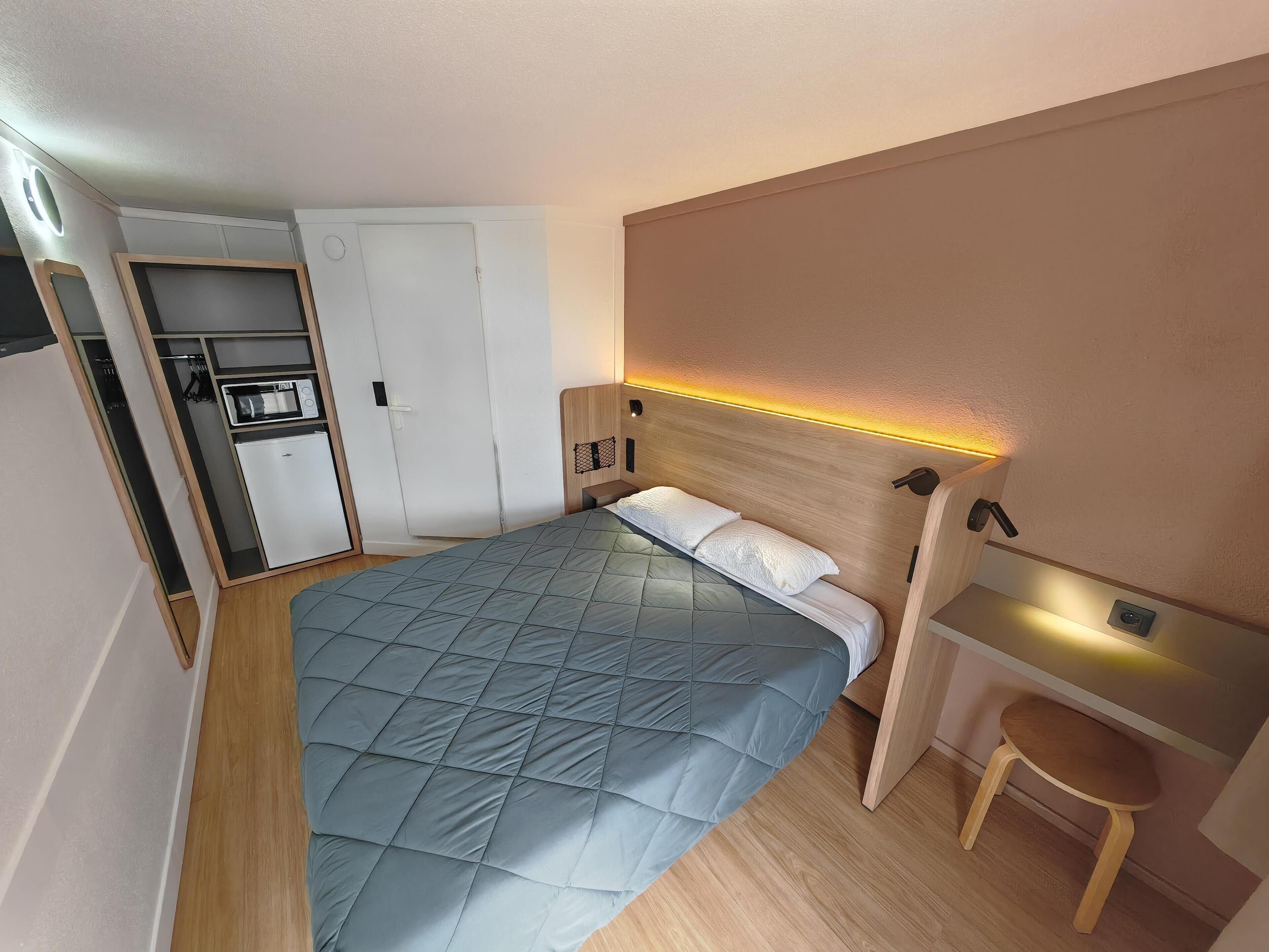 Une chambre à coucher de taille réduite, comprenant un lit, un petit bureau et une armoire intégrée.