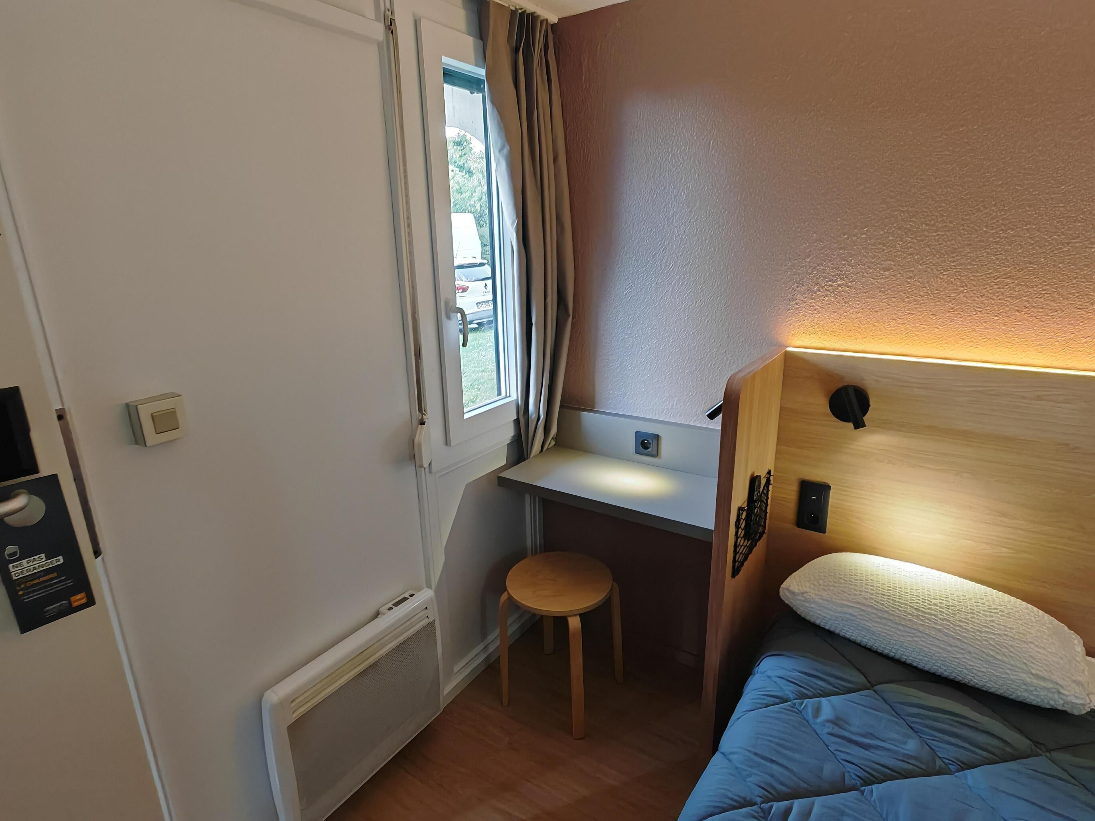 A compact room with a bed, a small desk, and a window.