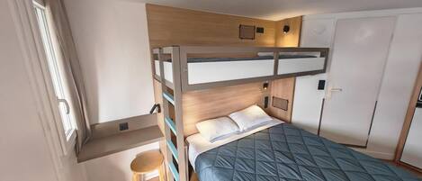 A bunk bed room with a desk and chair, a wardrobe, and a window.