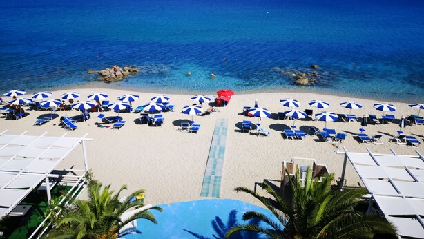 A beach with clear blue water, numerous umbrellas, and lounge chairs. - San Domenico Hotel (Soverato)