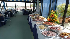 A buffet setup with various food items, tables with chairs, and a view of the sea through large windows. - San Domenico Hotel (Soverato)
