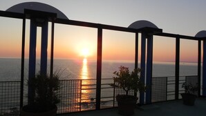 A balcony with a view of the sunset over the sea, potted plants, and a metal railing. - San Domenico Hotel (Soverato)