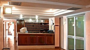 A hotel lobby with a reception desk, a patterned rug, a large window, and a wall of framed certificates. - San Domenico Hotel (Soverato)