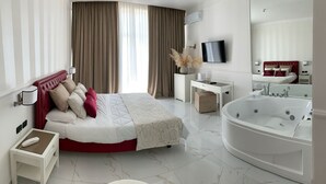 A modern hotel room with a large bed, a separate desk, a large bathtub, and a TV mounted on the wall. - Hotel Gli Dei (Pozzuoli)