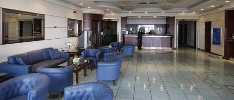 A hotel lobby with blue leather sofas, a reception desk, and a tiled floor.