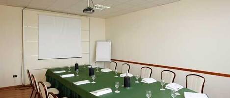 Ein Konferenzraum mit einem langen Tisch, Stühlen, einem Projektor und einer Tafel.