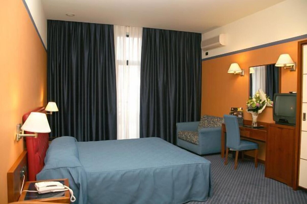 A hotel room with a bed, a desk with a chair, a television, and a lamp.