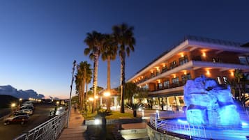 Un hotel con piscina, palmeras y una gran formación rocosa iluminada.