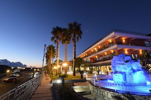 Un hotel con piscina, palmeras y una gran formación rocosa iluminada.