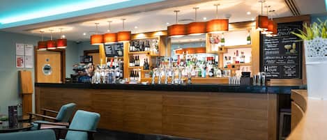 A bar area with a wooden counter, seating, and a menu board.