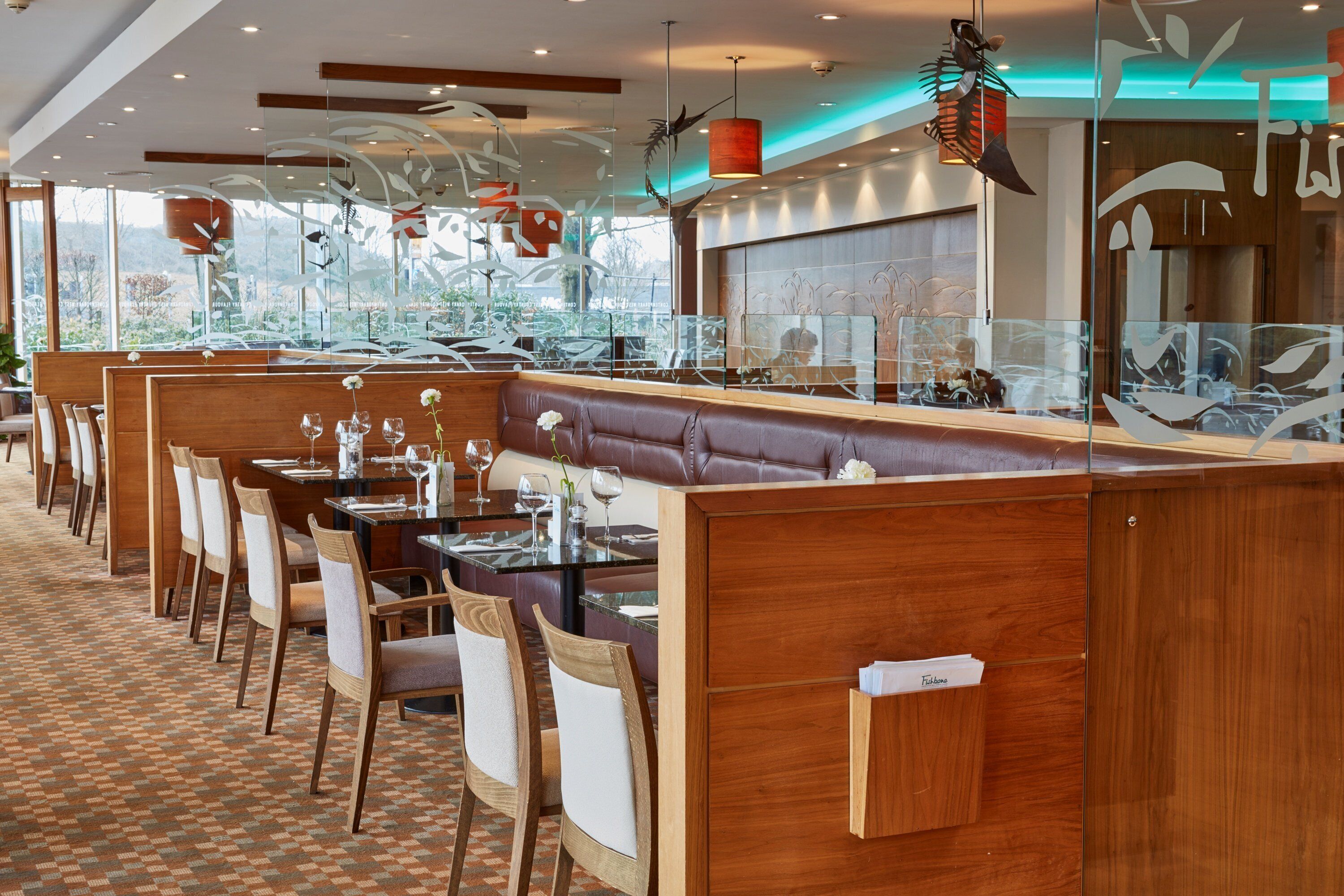 A modern restaurant with wooden booths, glass partitions, and a patterned floor.