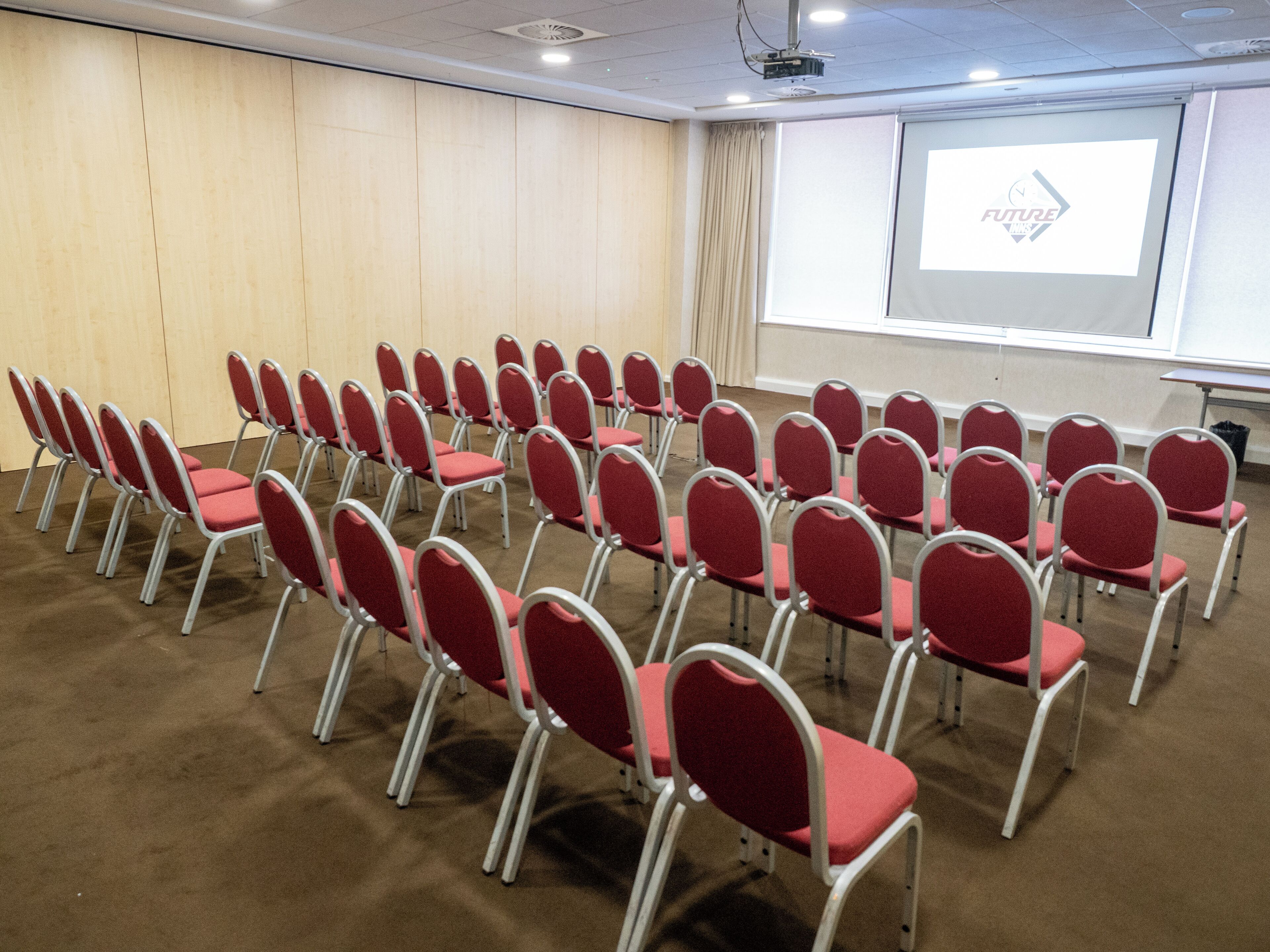 A conference room with rows of red chairs, a projector screen, and a large window.