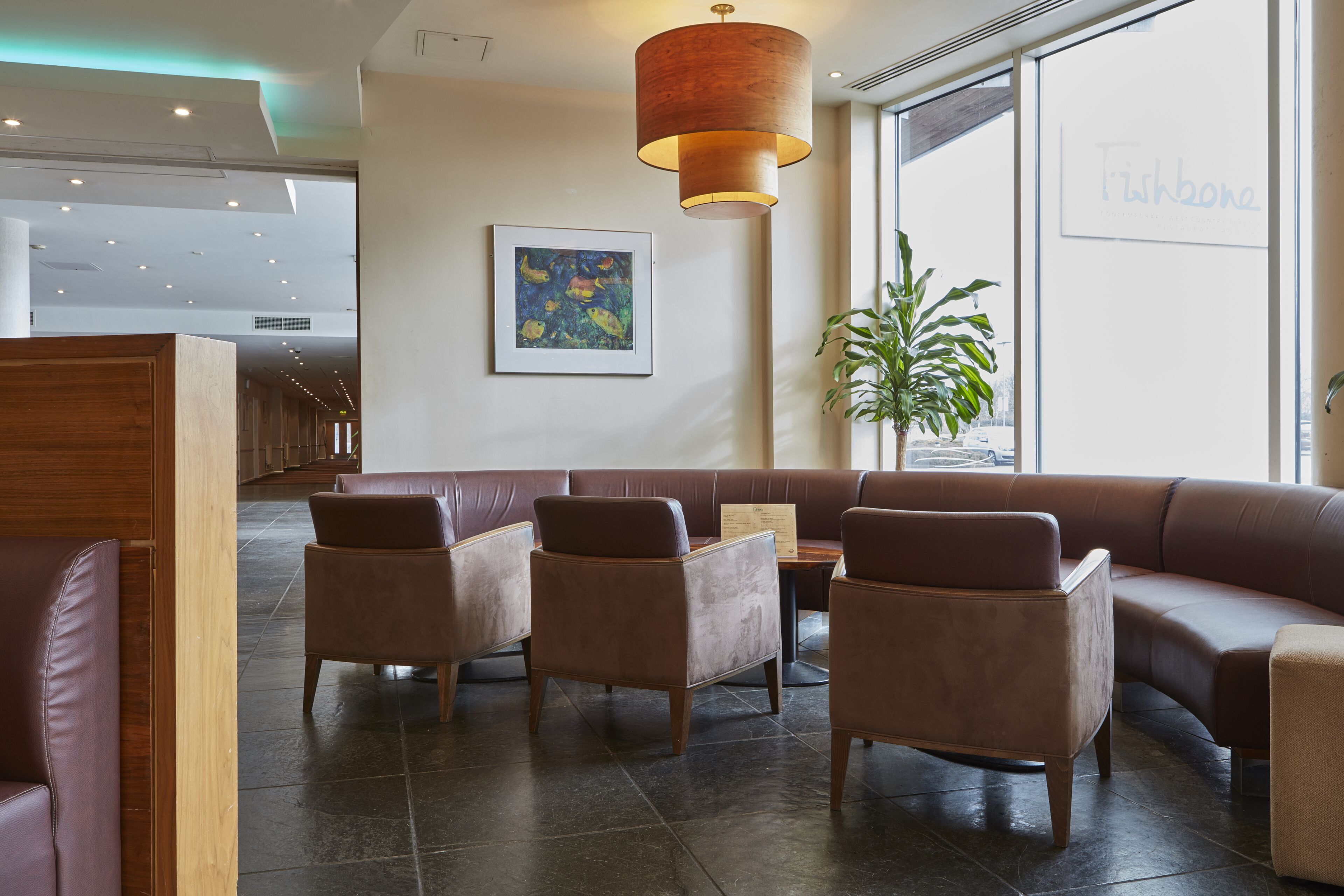 A modern interior with a seating area featuring leather sofas and armchairs, a tall floor lamp, and a large window with a view.