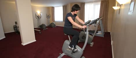 A room with a red carpet, an exercise bike, and a stationary bike.