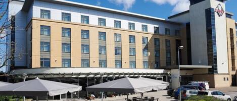 A hotel with a modern facade, multiple windows, and outdoor seating with umbrellas.