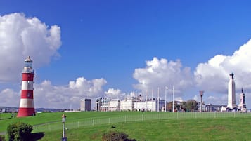 A lighthouse, a clock tower, and a building with flags in a grassy area.